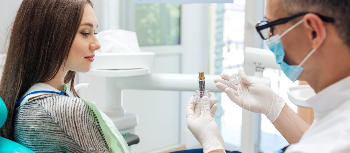 Male dentist showing his female patient a dental implant